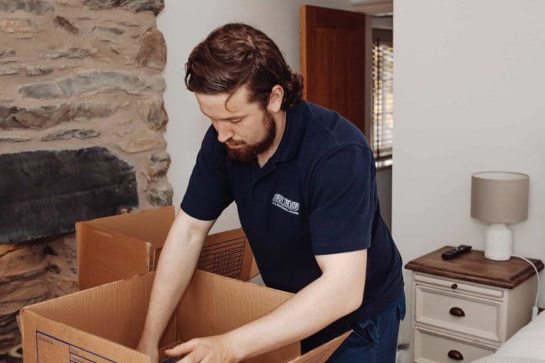 A guy with blue shirt is packing up all stuffs to move out into the big storage box