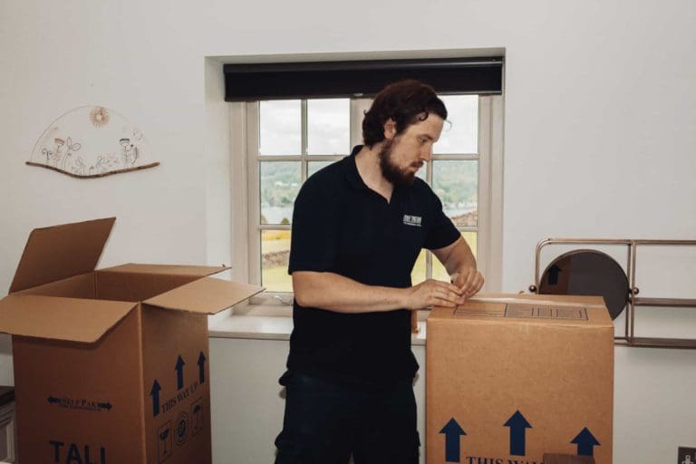 A man in black shirt and pants packing up things and wrapping in a big storage box