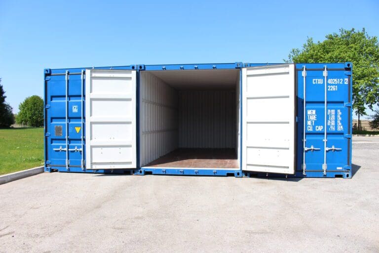 Open blue storage container with white doors, showing empty interior on a paved area, with green grass and trees in the background under a clear sky.