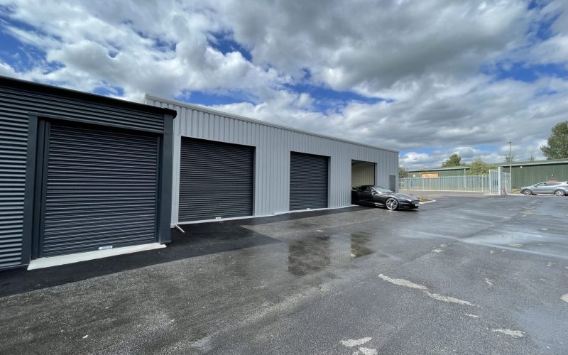 Exterior of Winsford storage facility with multiple grey roller door units, one open with a black car parked inside, under a cloudy sky.